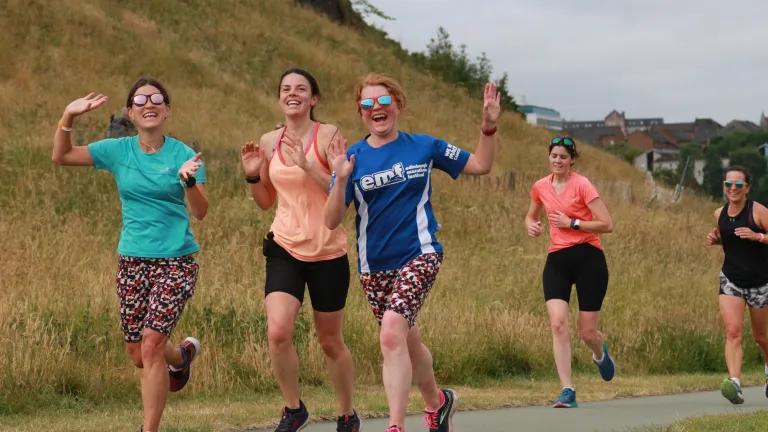 Participants to the 2022 Holyrood Parkrun smiling and waving during the race.