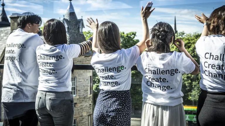 Five students standing on the roof terrace. They wear white t-shirts that read Challenge, Create, Change on the back.
