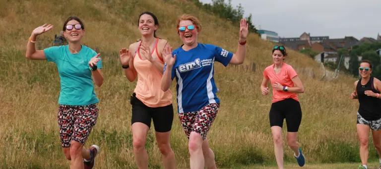 Participants to the 2022 Holyrood Parkrun smiling and waving during the race.