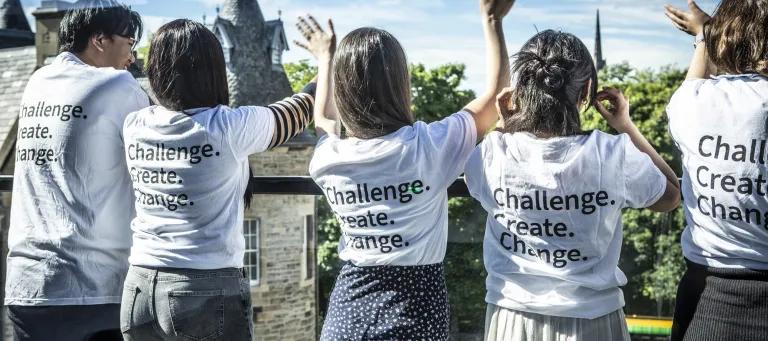 Five students standing on the roof terrace. They wear white t-shirts that read Challenge, Create, Change on the back.